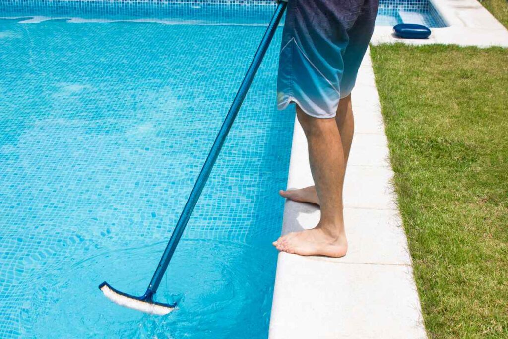 Homme qui nettoie l'eau de la piscine avec une brosse